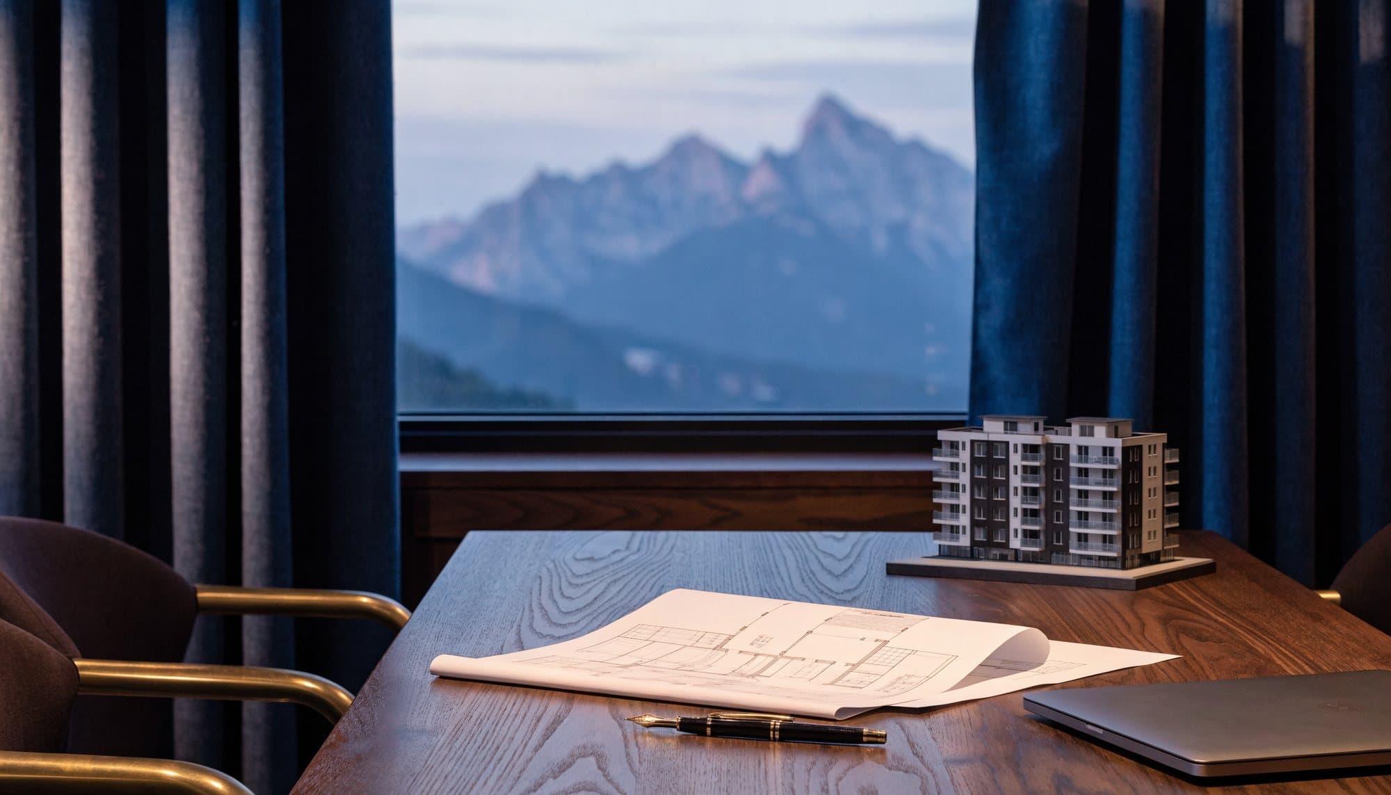 Table de travail avec des plans d’architecte et une maquette d’immeuble, face aux montagnes