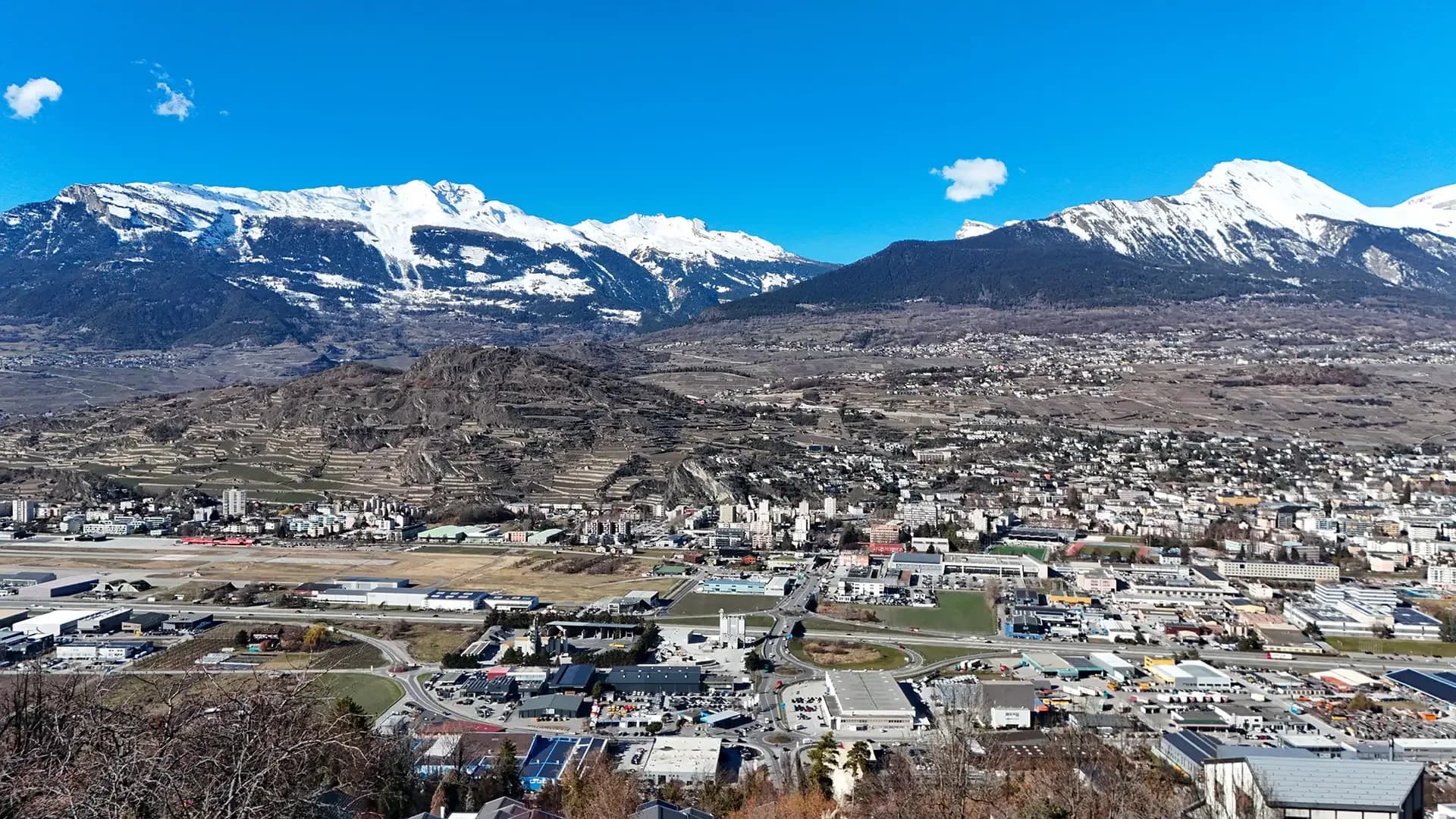 La vallée de Sion vue depuis les hauteurs, sous un ciel dégagé, sommets enneigés à l’arrière-plan