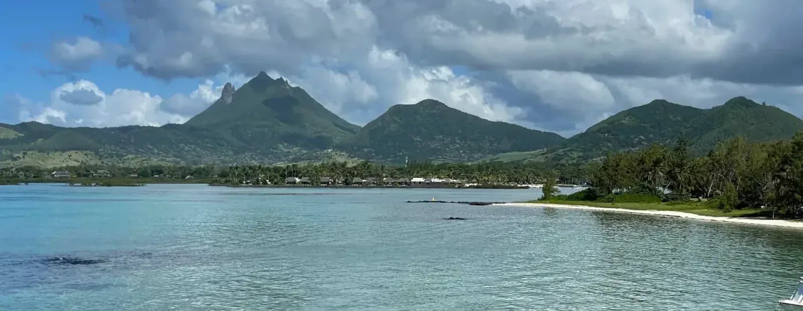 Lagon turquoise de la côte est de l’île Maurice, plage bordée de palmiers et montagnes en arrière-plan